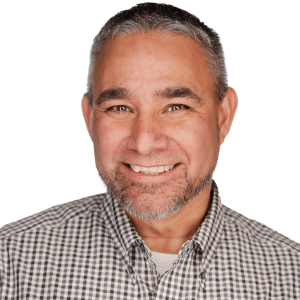 A smiling man with a beard in a checkered shirt against a white background.