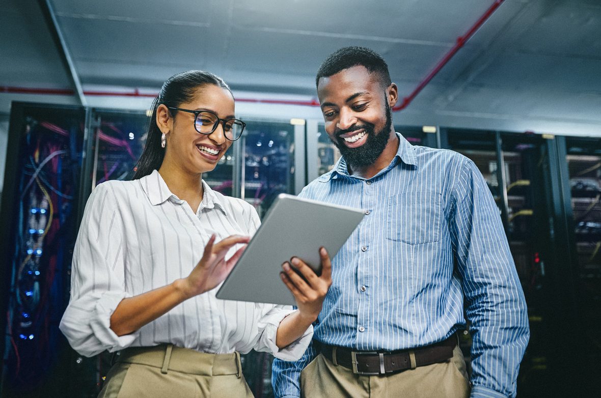 Two professionals reviewing data on a tablet in a server room.