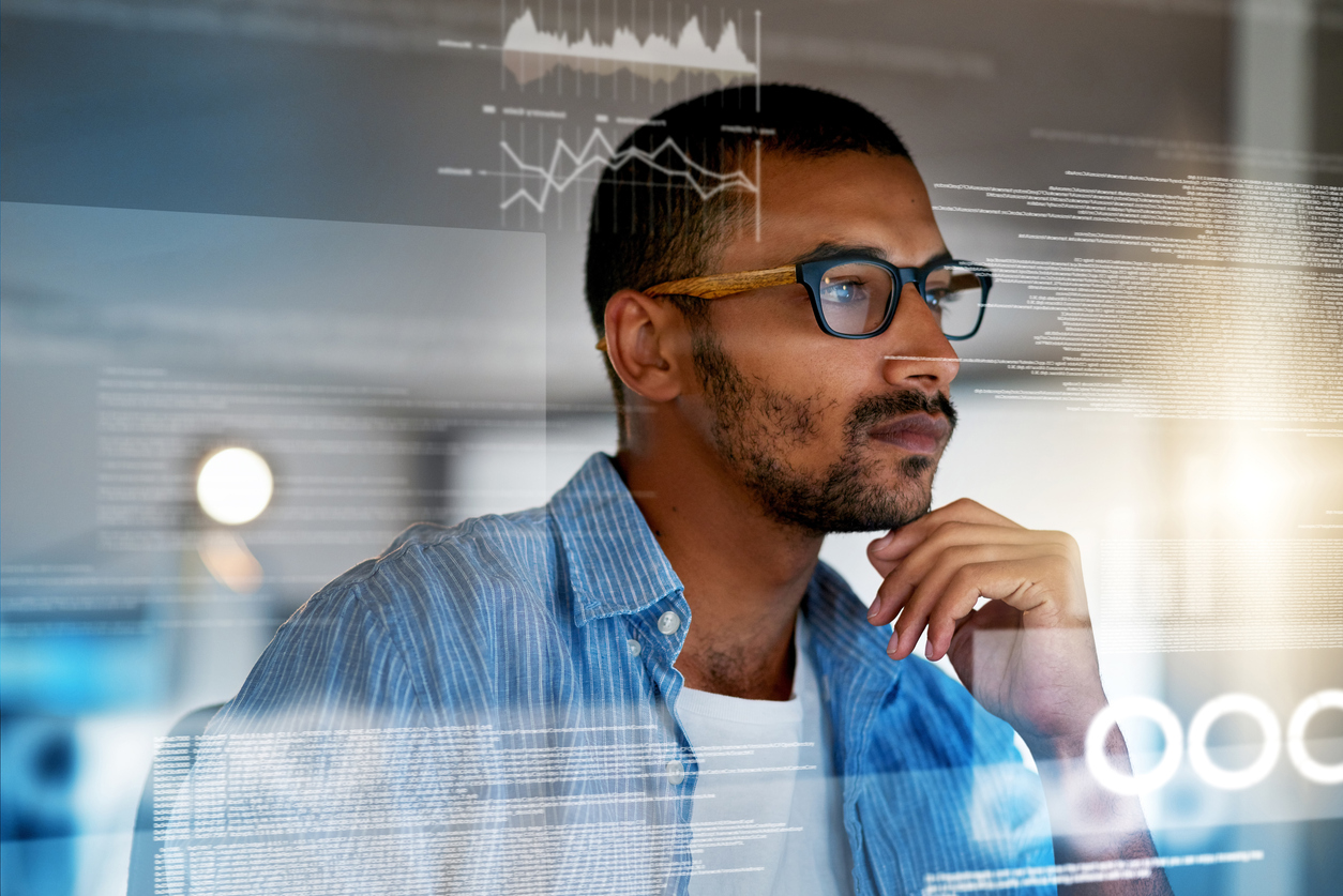 A man wearing glasses looks at data and graphs on a screen, contemplating and analyzing information.