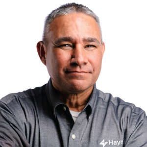 Man in a gray Haynes shirt with crossed arms against a white background.